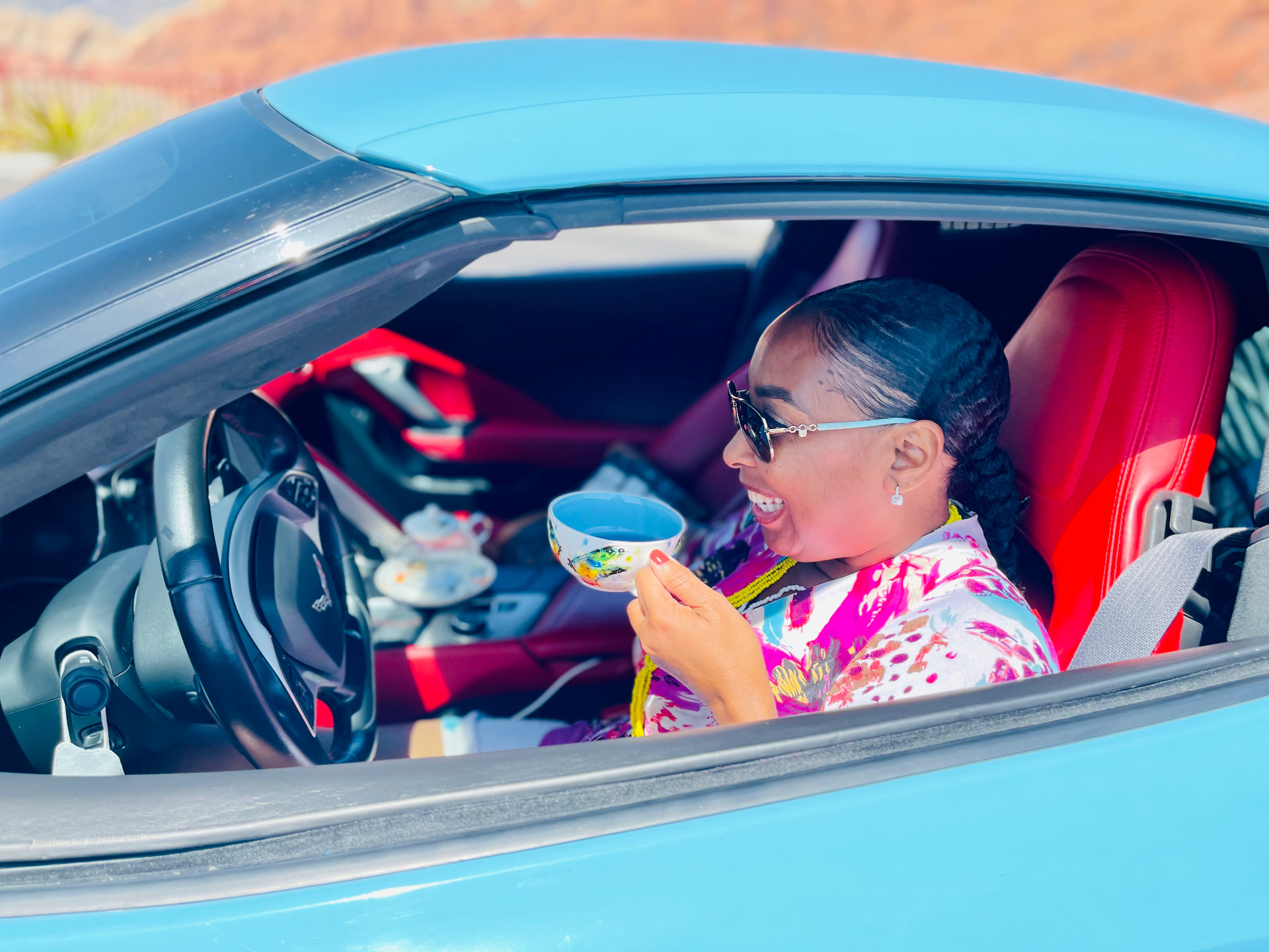 LaTanya Potts sipping tea from a hand-painted cup in a blue sports car